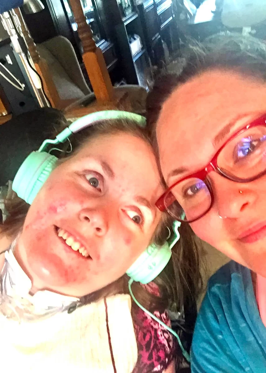 Angie and her Sister Becca Dingley at their family home in Cordova, SC. Both are smiling at the camera while Becca listens to her first Disability Justice Podcast.